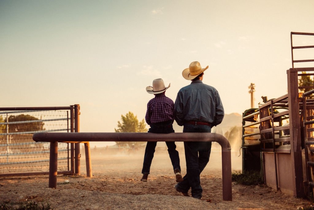 Two cowboys standing at a ranch fence, symbolizing the strong foundation and tradition behind the Boot N Shoot business model.