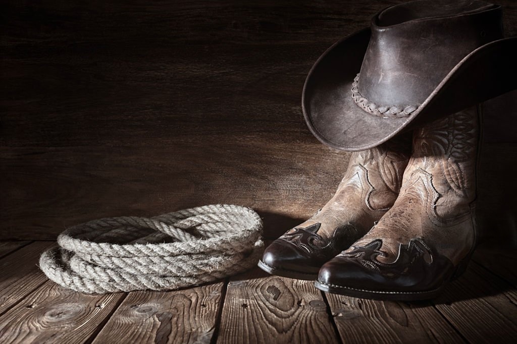 Western cowboy hat, leather boots, and rope on wooden floor symbolizing the Boot N Shoot franchise’s strong brand identity.