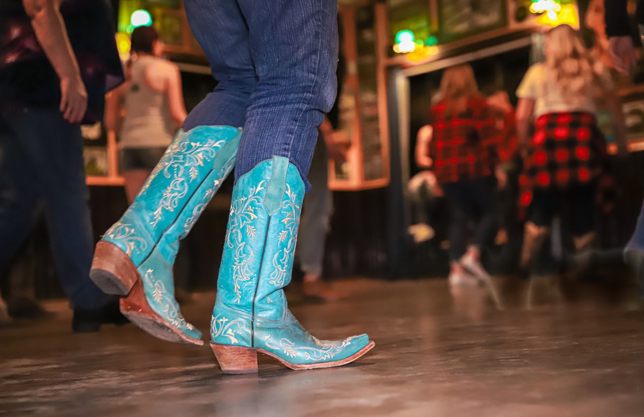 Person wearing turquoise cowboy boots dancing on a wooden floor.