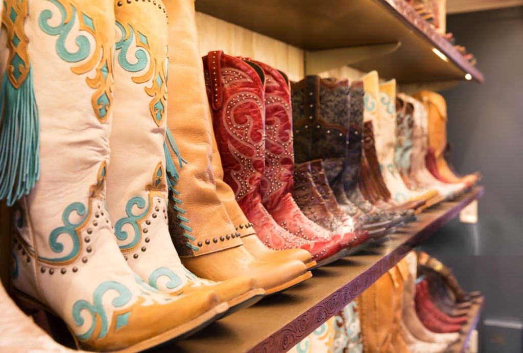Rows of colorful cowboy boots displayed on wooden shelves in a Western wear store. 