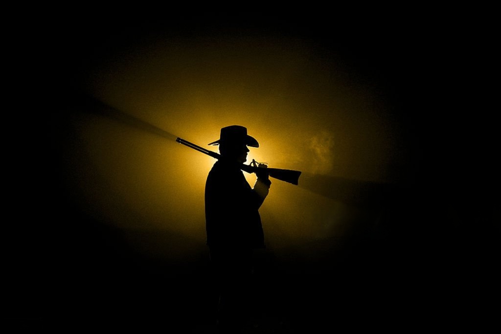 Silhouette of a cowboy holding a rifle at sunset, representing the Western spirit and Boot N Shoot lifestyle.