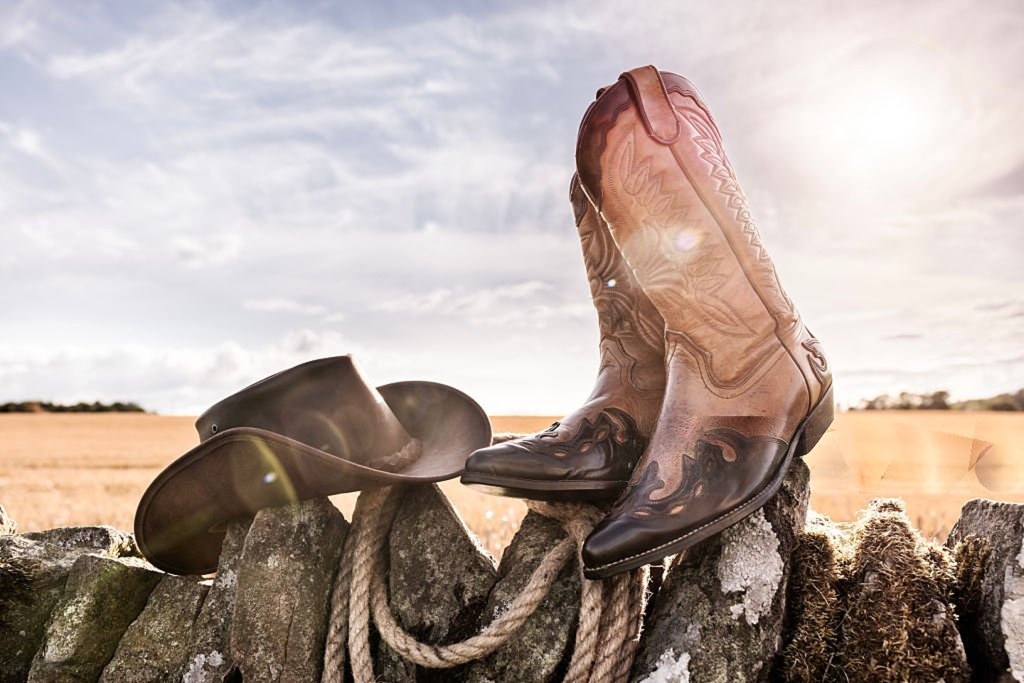 Feature image Cowboy boots and hat on a stone fence in a sunny field