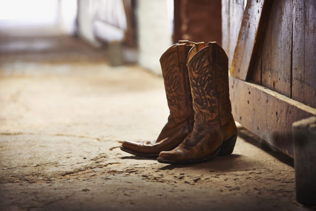 Pair of worn brown cowboy boots on a dusty barn floor.