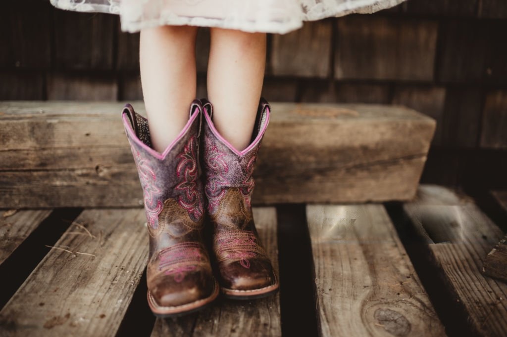 Feature image Boot N Shoot Child wearing brown and pink cowboy boots standing on wooden steps.